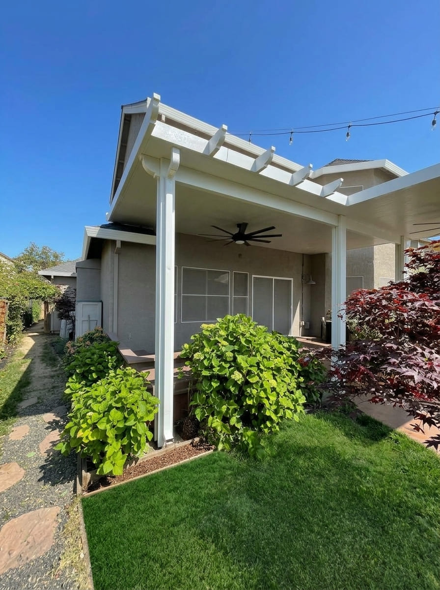 Attached solid insulated aluminum patio cover with decorative scalloped corbel rafter tails, integrated large outdoor ceiling fan, and rain gutters over a backyard patio in Loomis, CA.