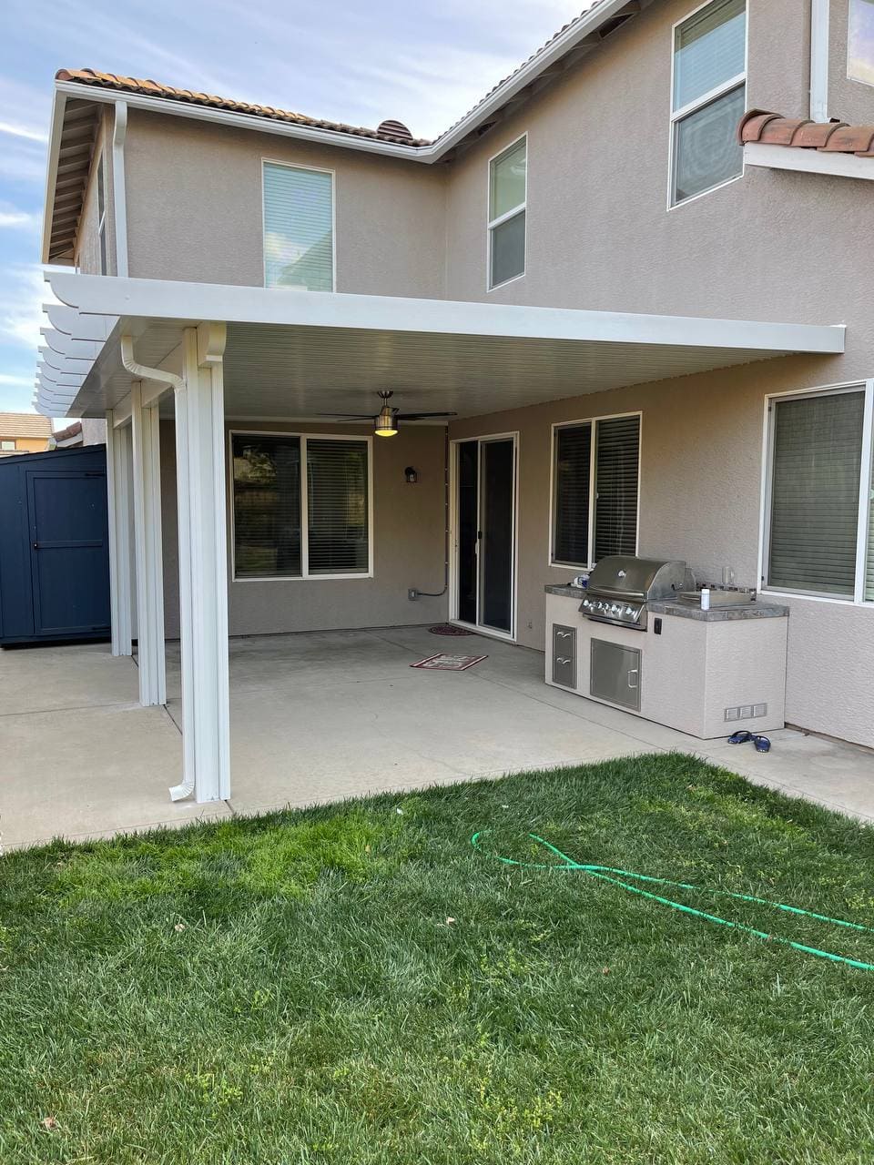 Custom attached solid insulated aluminum patio cover featuring an integrated ceiling fan with lighting shading an outdoor built-in BBQ grill island over a concrete patio in Roseville, CA.