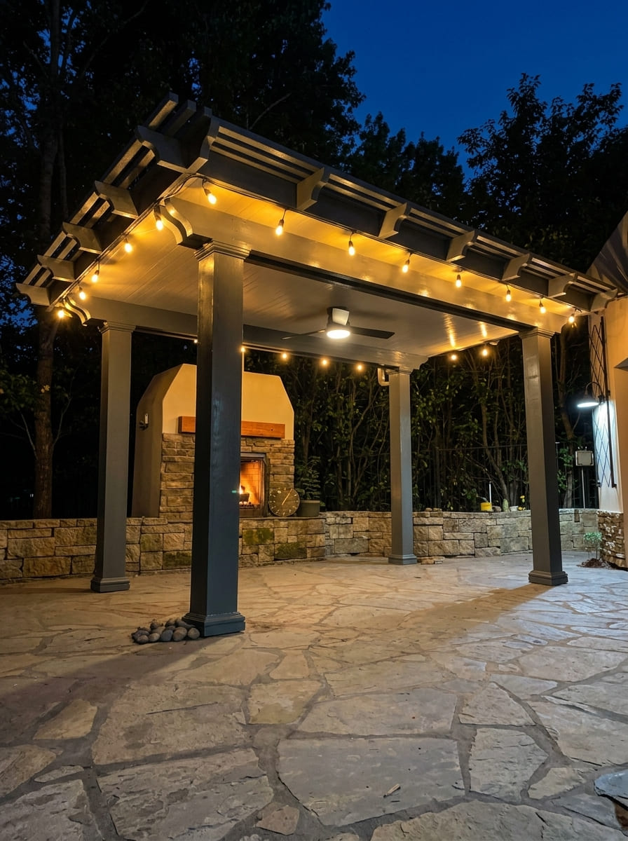 Freestanding solid insulated aluminum patio cover pavilion in dark charcoal finish with integrated ceiling fan, warm bistro lights, and outdoor stone fireplace on flagstone patio in Granite Bay, CA.
