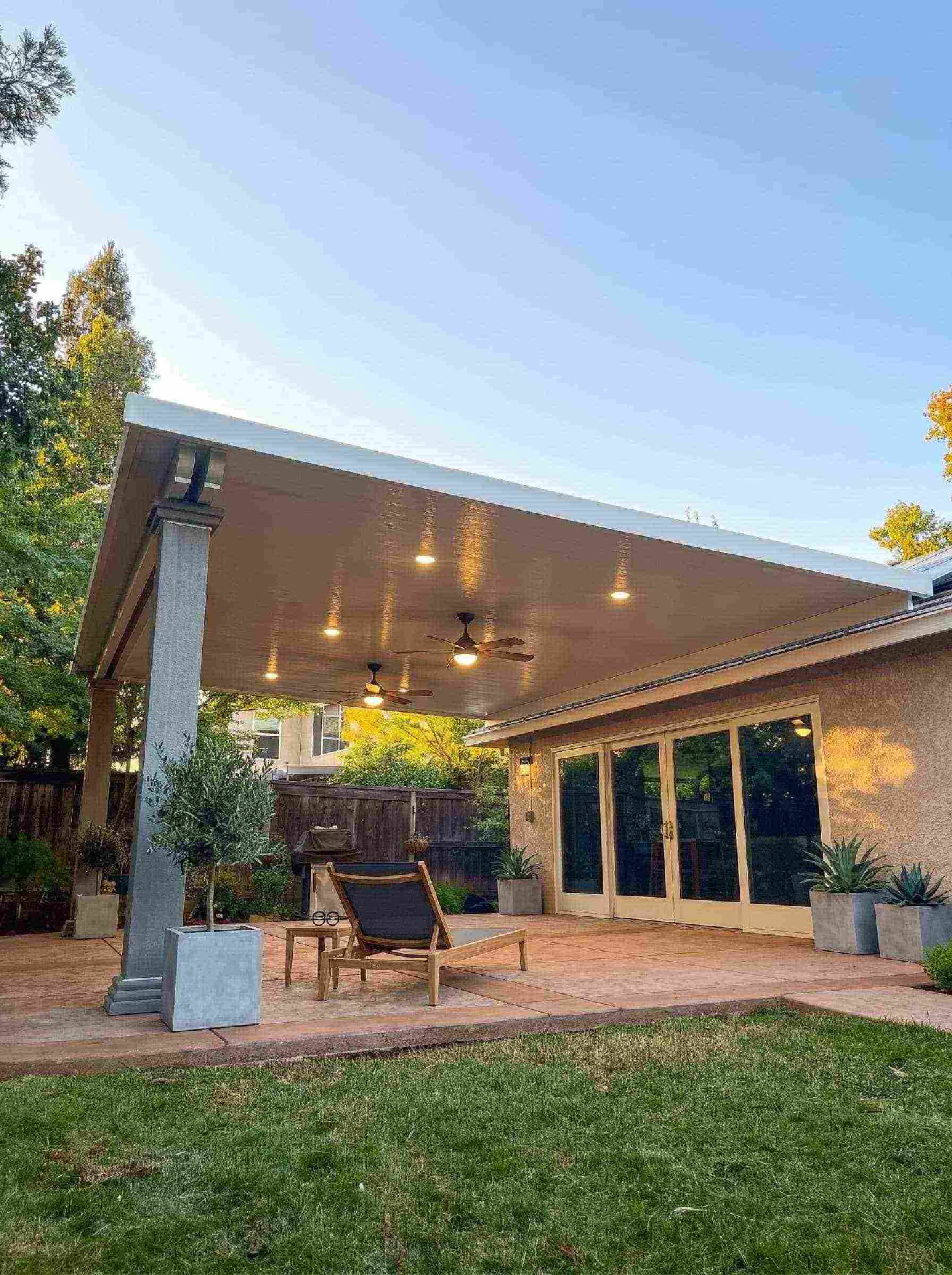Large attached solid insulated aluminum patio cover with recessed LED pot lighting, dual ceiling fans, and custom architectural column over a stamped concrete patio in Fair Oaks, CA.