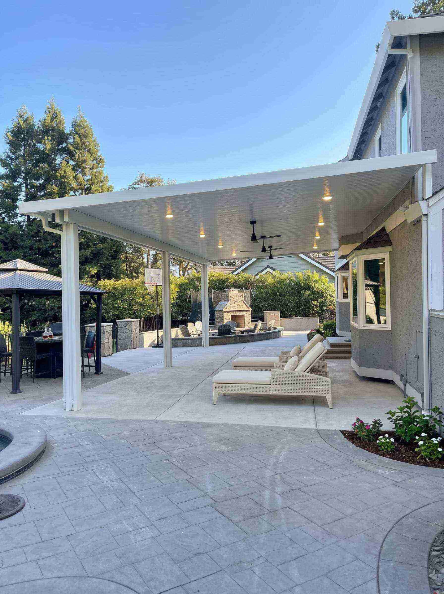 Spacious attached solid insulated aluminum patio cover with integrated recessed LED pot lighting, dual ceiling fans, and poolside lounge seating overlooking an outdoor fireplace in Loomis, CA.