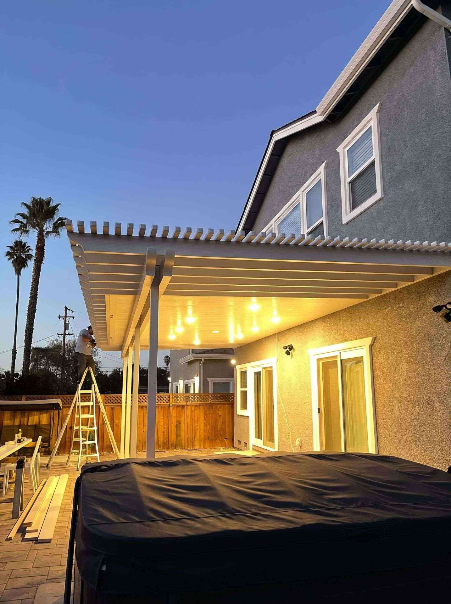Custom attached combo patio cover featuring an insulated solid roof with glowing warm recessed LED pot lights and open lattice pergola trim over a hot tub spa patio at dusk in Citrus Heights, CA.