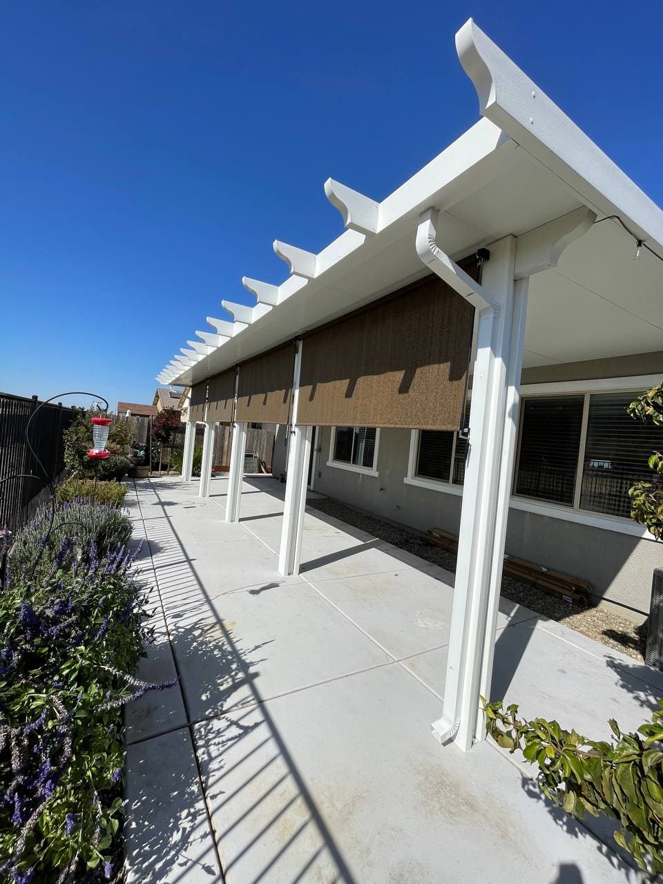 Custom attached solid aluminum patio cover with decorative corbel rafter tails and integrated outdoor retractable solar drop shades installed on a concrete patio in Lincoln, CA.