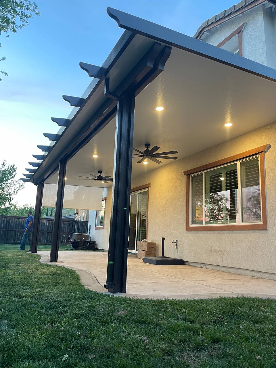 Attached solid insulated aluminum patio cover in two-tone dark bronze finish featuring decorative corbel rafter tails, recessed LED pot lights, ceiling fans, and retractable solar drop shades in Roseville, CA.